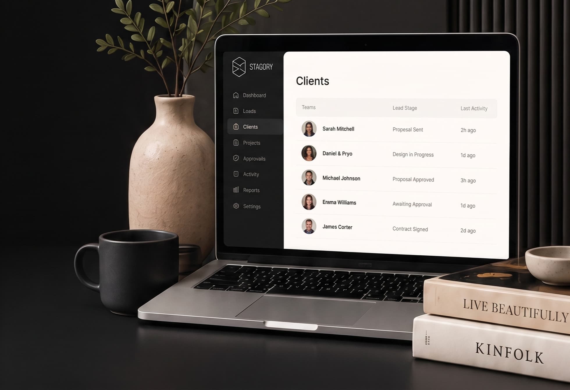 A designer's workspace — open laptop showing the Stageory Clients dashboard with leads, lead stages, and last-activity timestamps, alongside a ceramic vase and books on a dark desk